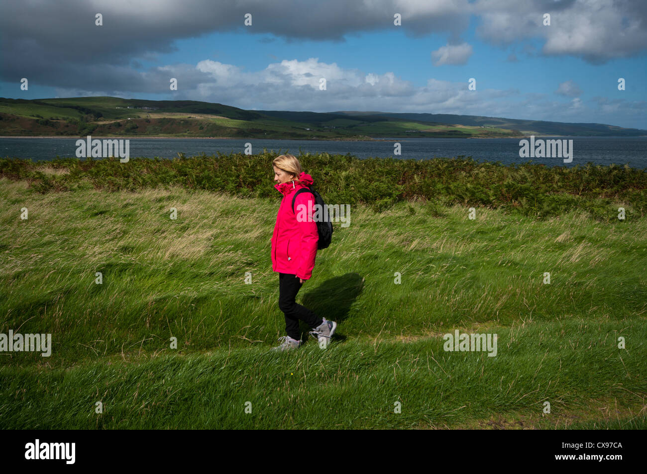 Side View Of A Woman Person Walking Through The Countryside Wearing Waterproof Clothing and A Rucksack Stock Photo