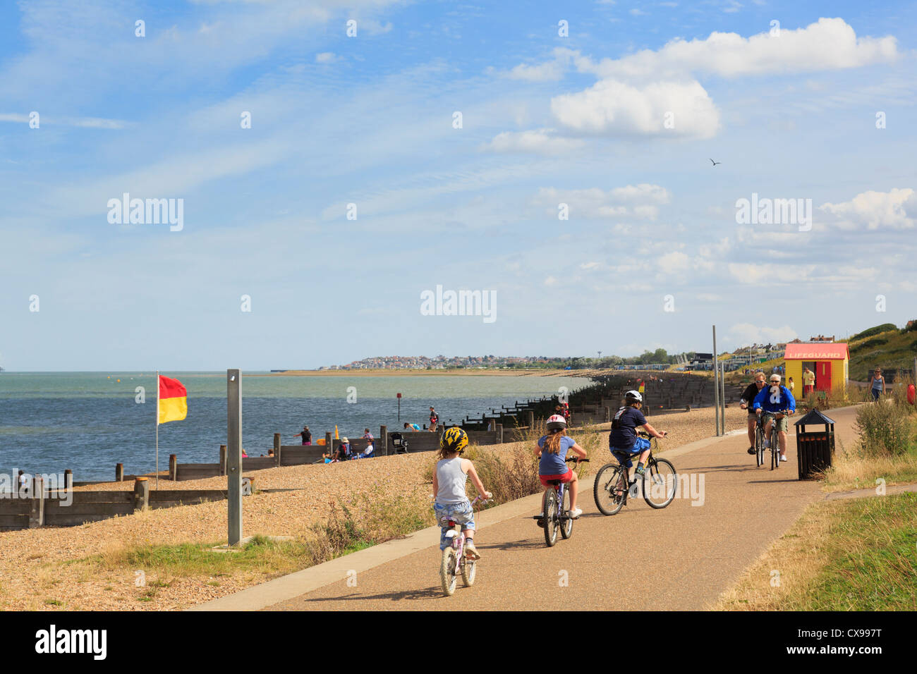 People cycling on Whitstable seafront promenade along Saxon Shore Way in Tankerton Bay to Swalecliffe on north Kent coast. Whitstable Kent England UK Stock Photo