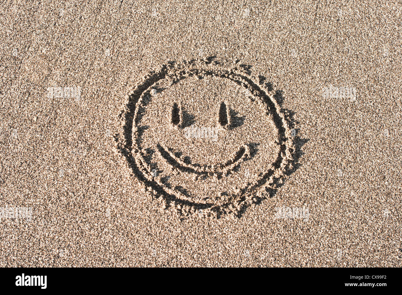 Smiley face drawn on beach sand Stock Photo