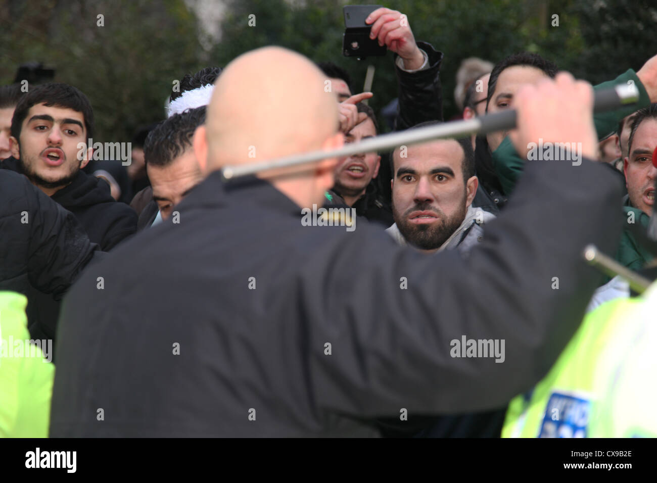 A police officer raises his baton to anti Syrian President Assad protesters outside the Syrian Embassy London. Stock Photo