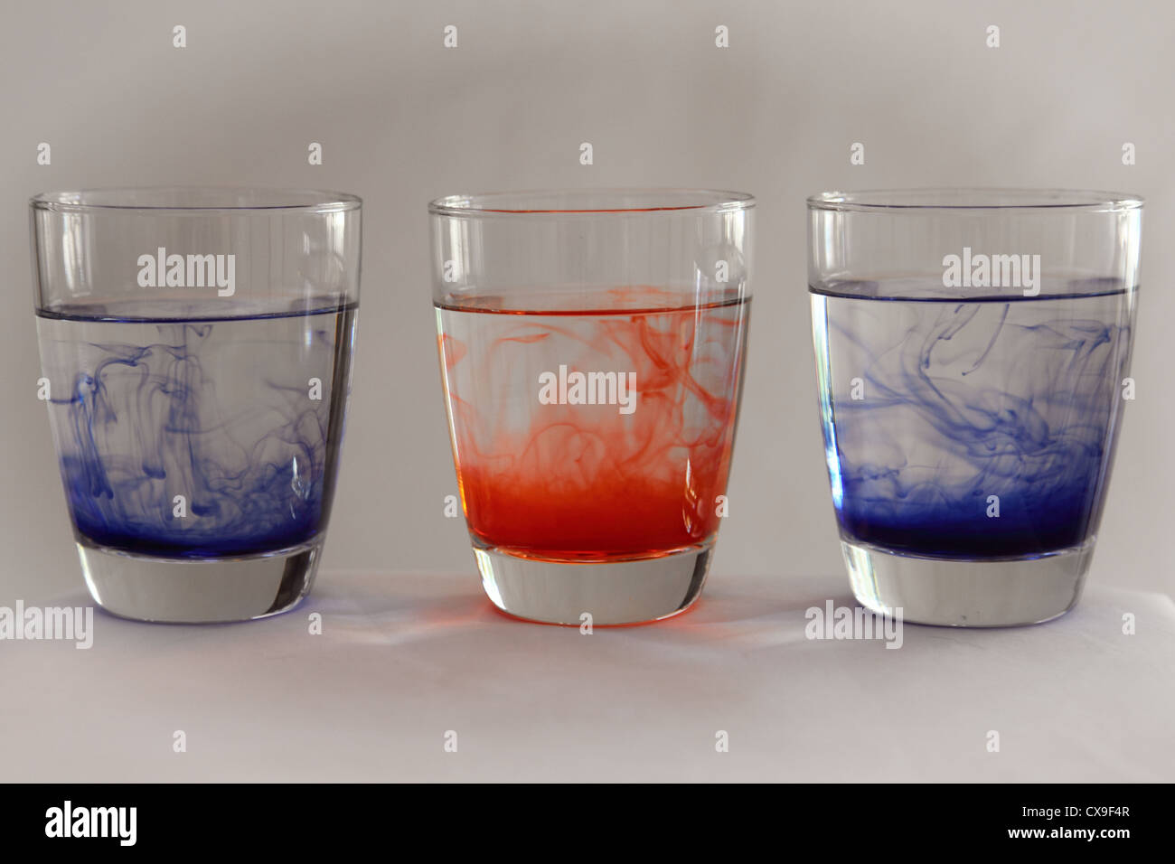 Red and blue ink floats through three glasses of water. Stock Photo