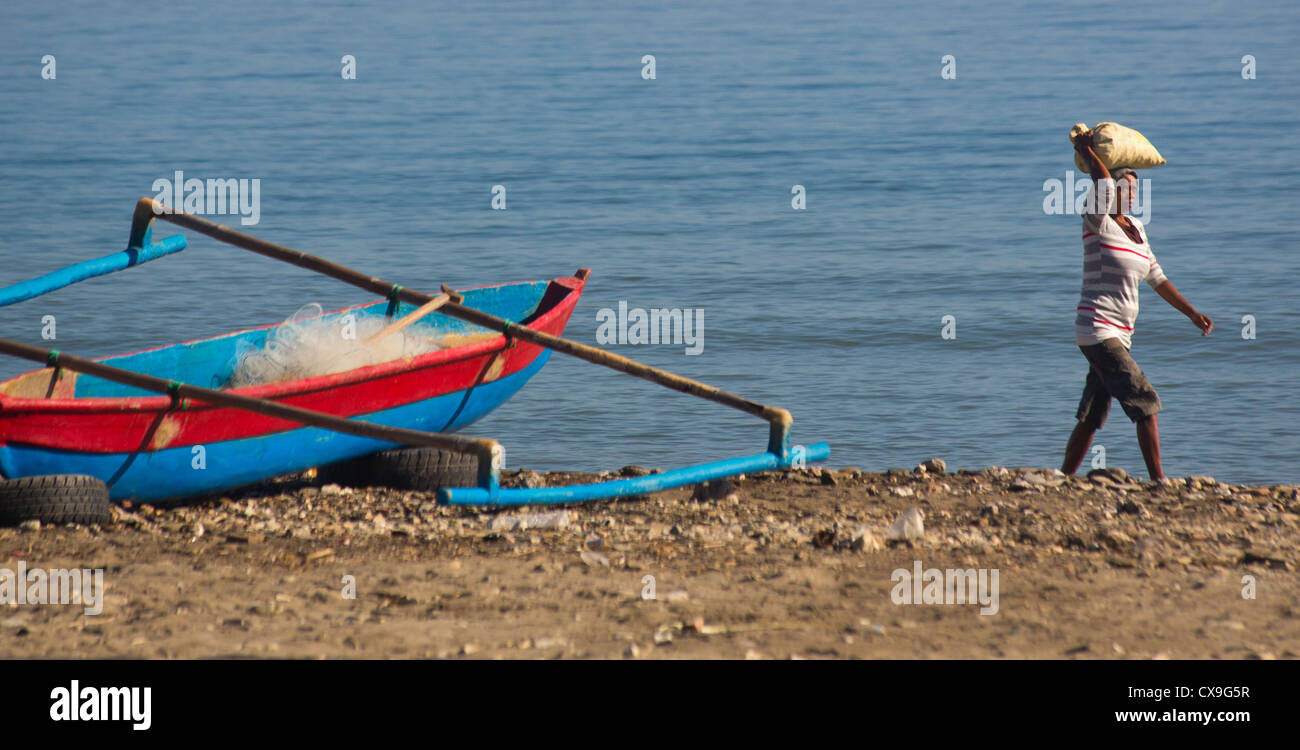 Woman carrying a bag of stones on her head on a beach, Dili, East Timor Stock Photo