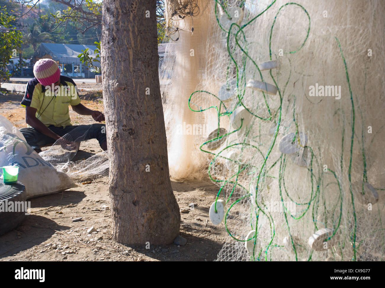 Man mending his fishing nets on a beach, Dili, East Timor Stock Photo