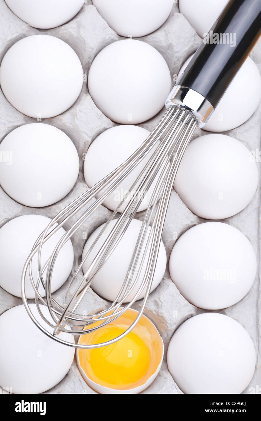 Whisk on eggs in carton with one broken showing the yolk Stock Photo