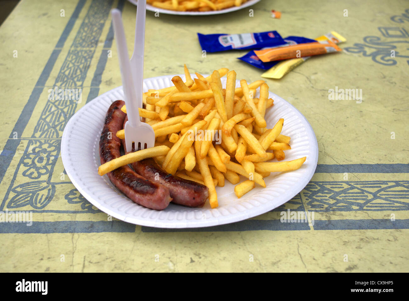 Sausages and chips on a paper plate with plastic cutlery, France. Stock Photo