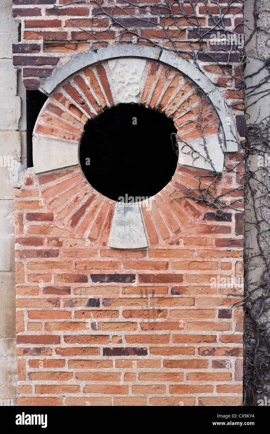 An old red brick wall recently cleared of climbing plants, with a circular opening. Stock Photo