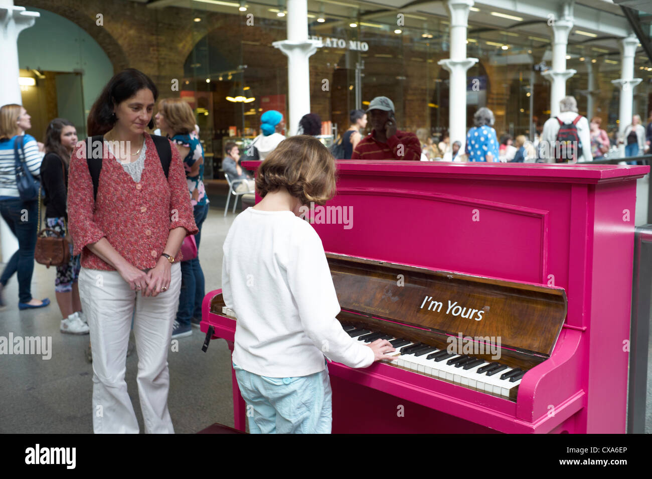 A child plays the public piano at St Pancras train station, London UK Stock Photo