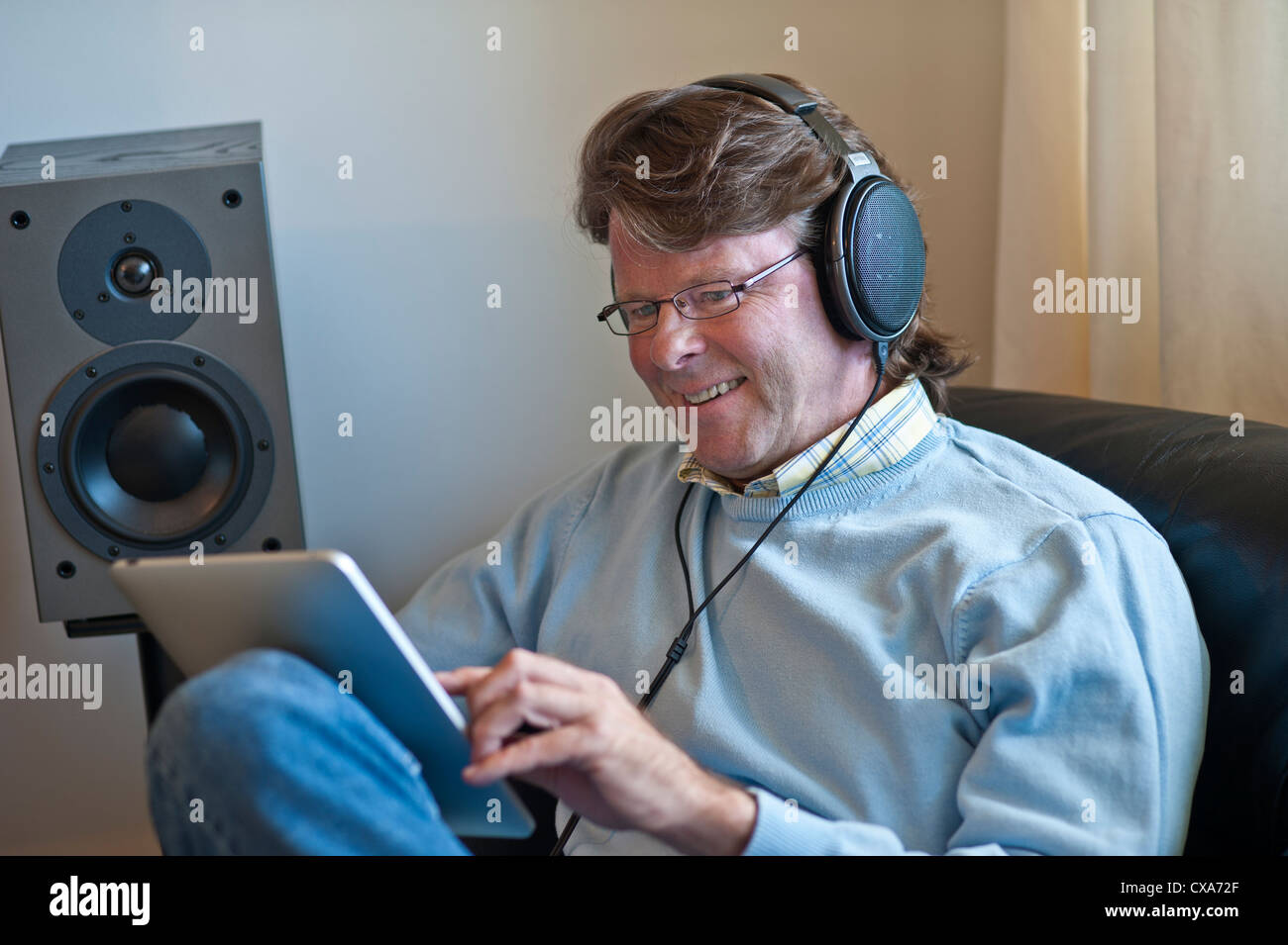 Mature man at home listening with headphones to his iPad tablet computer in contemporary living room Stock Photo