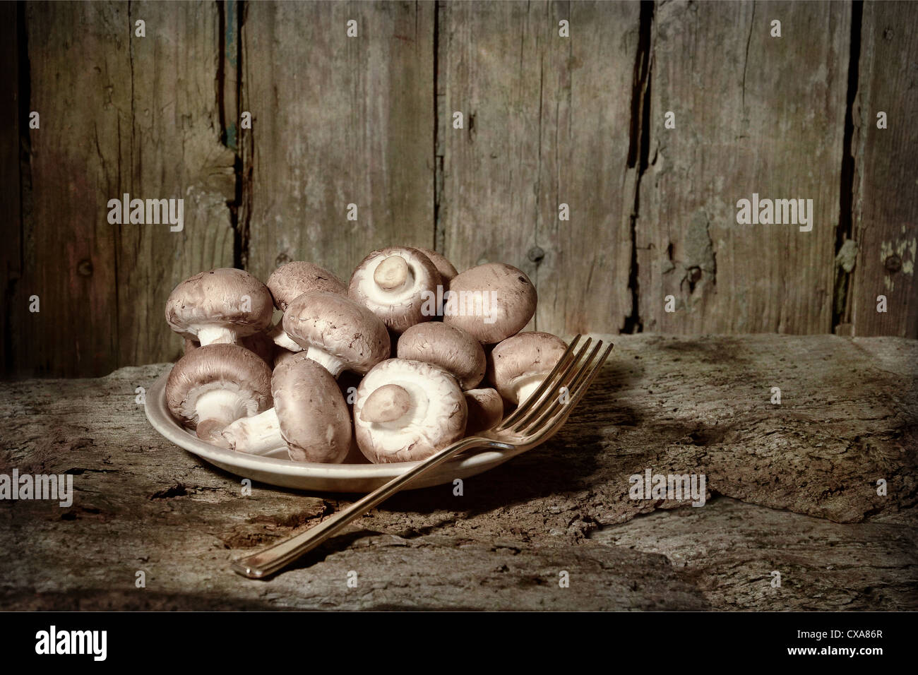 fungi organic produce button brown mushrooms uncooked in a plate ready picked with fork ready to be cooked eaten food old table Stock Photo