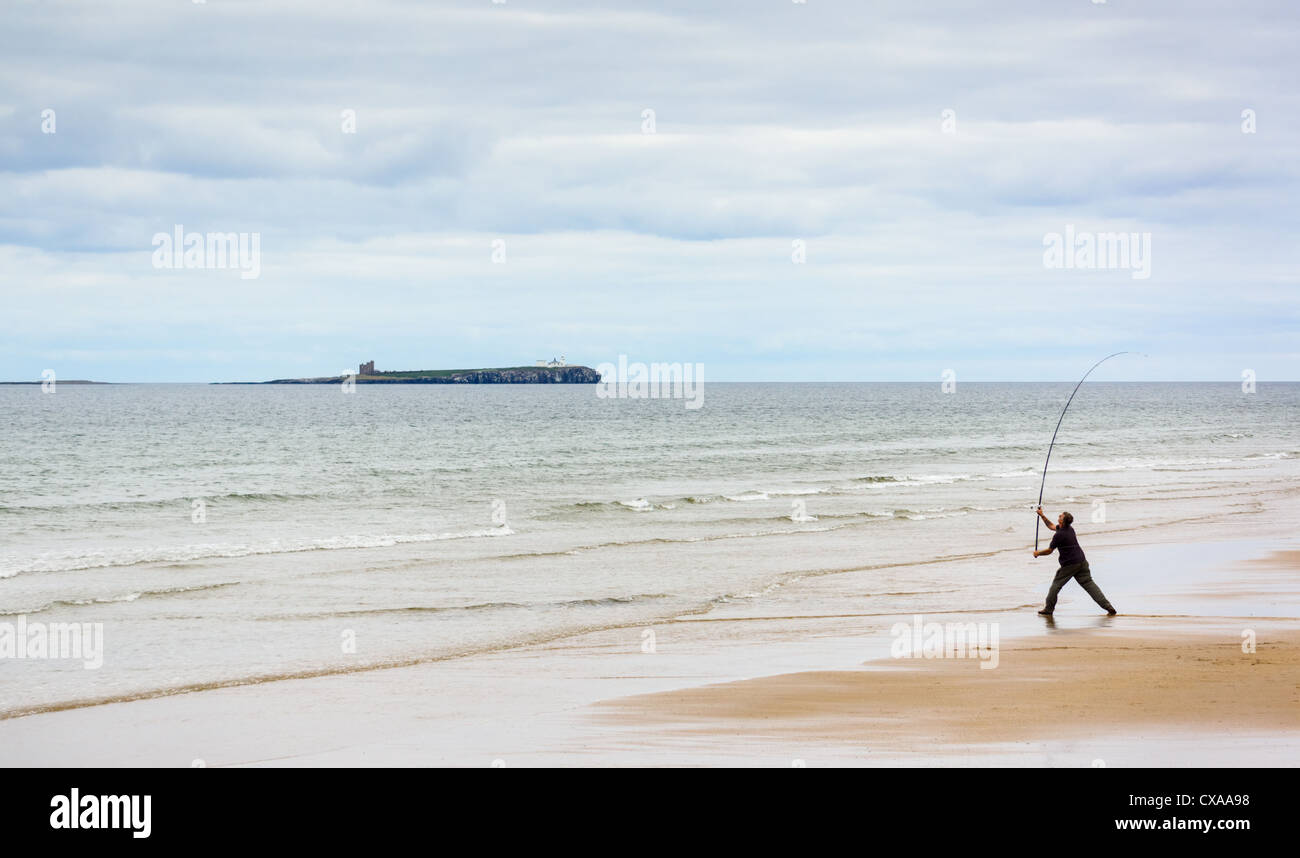A fisherman casting his rod out to see from Bamburgh Beach in Northumberland. Stock Photo