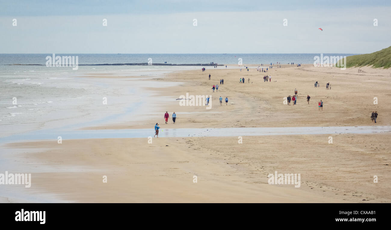 Tourists out walking and relaxing on the wide sands of Bamburgh Beach in Northumberland. Stock Photo