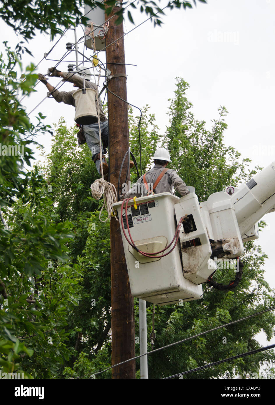 One man inside a lift bucket helps another man on a power pole install new electrical lines in Oklahoma City, Oklahoma. USA. Stock Photo