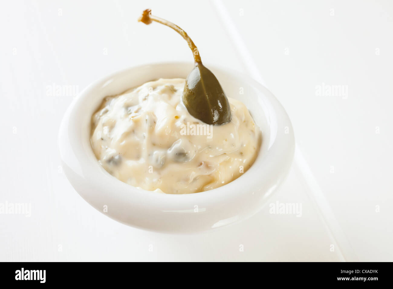 A small bowl of homemade tartare sauce with a caperberry. Stock Photo