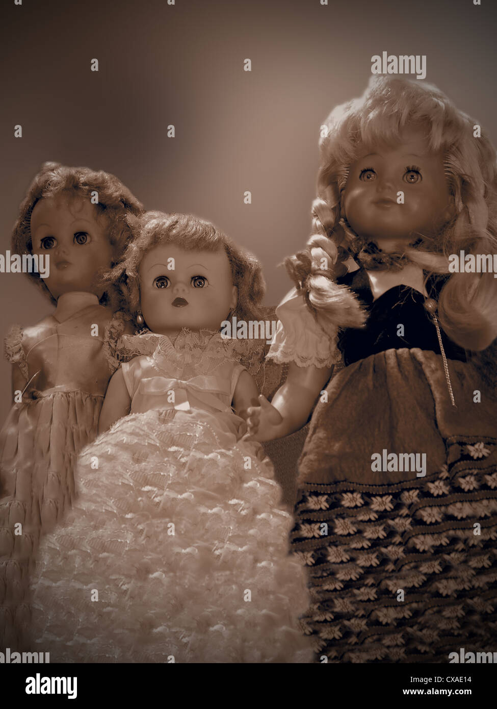 A trio of beautiful vintage dolls in sepia tone stands above the viewer, against a soft background brown and cream background. Stock Photo