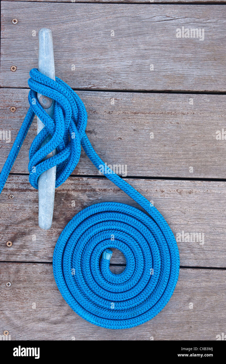 Blue rope coiled on a wooden dock and tied to a metal dock cleat. Cleats are used for securing docks and lines from boats Stock Photo