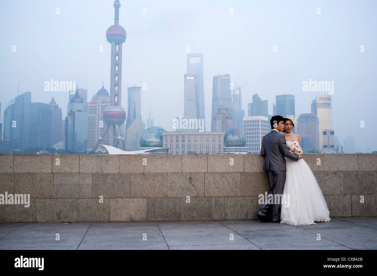 Young married couple posing for wedding photographs on The Bund with skyline of Pudong financial district  rear Shanghai China Stock Photo
