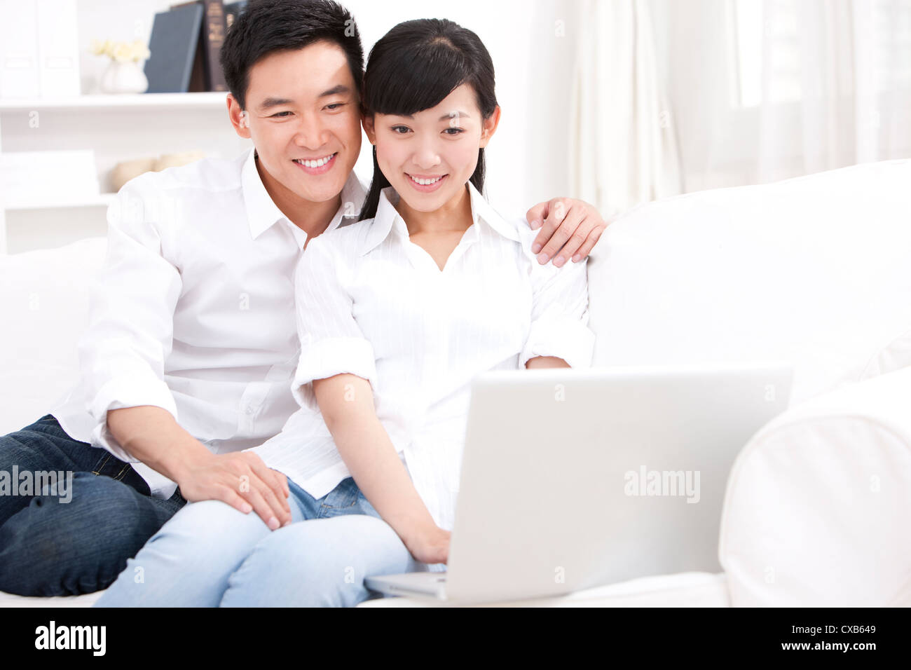 Young couple using laptop in sofa Stock Photo - Alamy