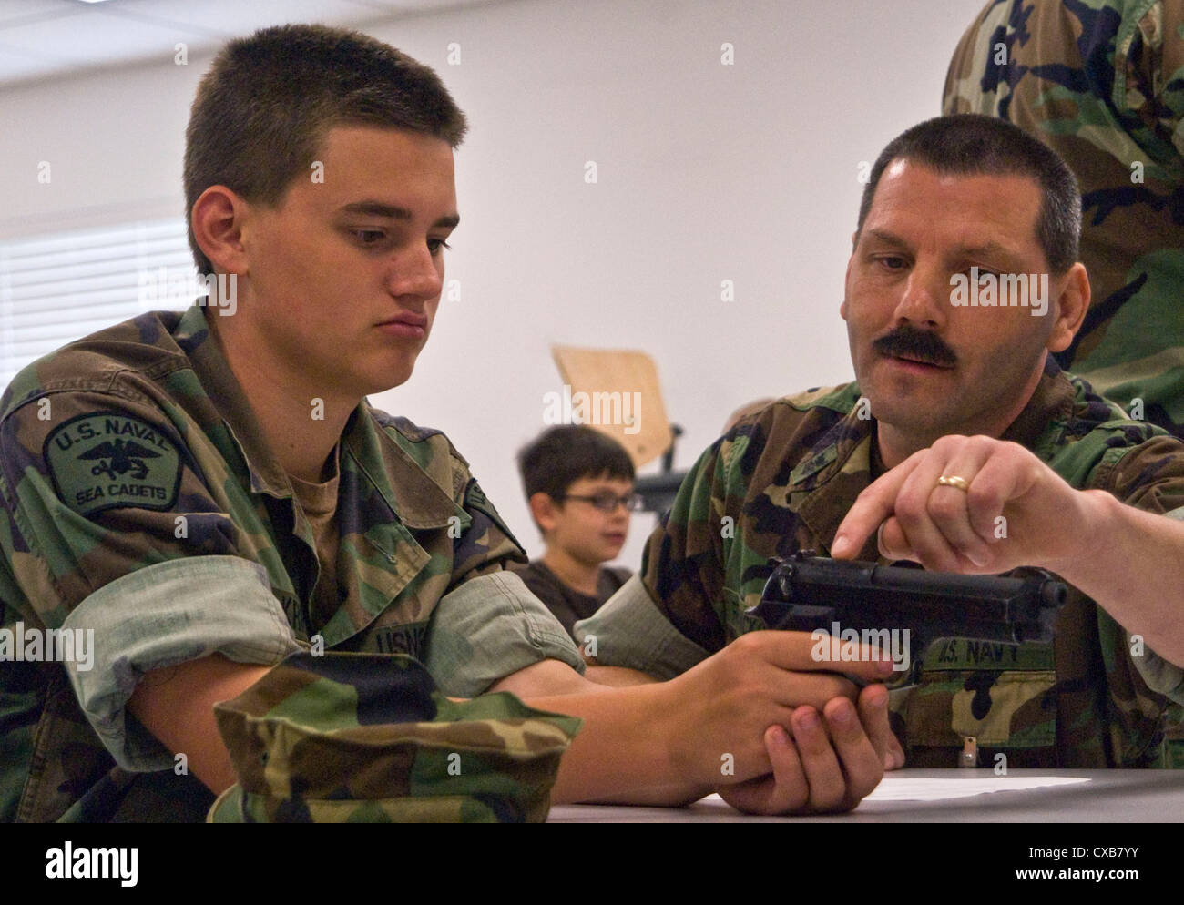 Petty Officer 1st Class Ken Franckowiak, weapons leading petty officer at Submarine Group (SUBGRU) 9 Force Protection Det. 1, shows the firing sequence of the M9 Beretta pistol to Seaman Daniel Krieg, a Cadet with the Navy Sea Cadet Corps, Kitsap Unit, during a weapons-familiarization class held by reserve component sailors at Naval Base Kitsap. The class was the first event in a new relationship between SUBGRU-9 sailors and the Sea Cadets. Stock Photo