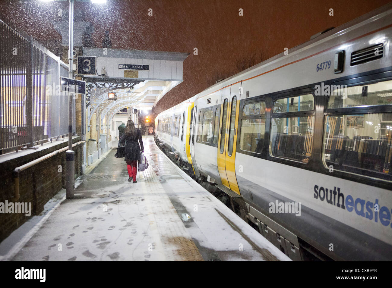Snowy platform, woman in red trousers and Southeastern train at Lewisham Station Stock Photo