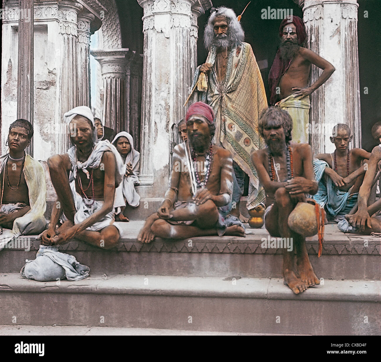 Colorized portrait of a group of pilgrims sitting on steps near the Ganges in Varanasi, also known as Benares, India, 1912. (Photo by Burton Holmes) Stock Photo