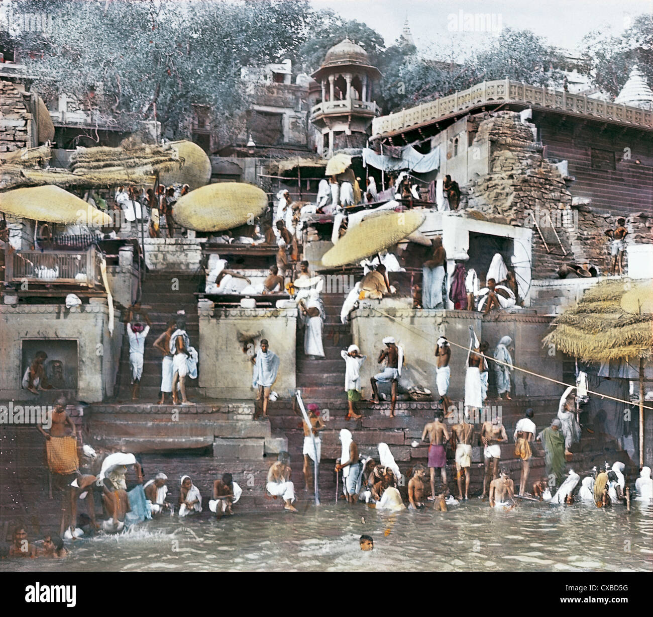 Colorized photo of pilgrims bathing in the Ganges and standing on a ghat in Varanasi, also known as Benares, India 1912. (Photo by Burton Holmes) Stock Photo