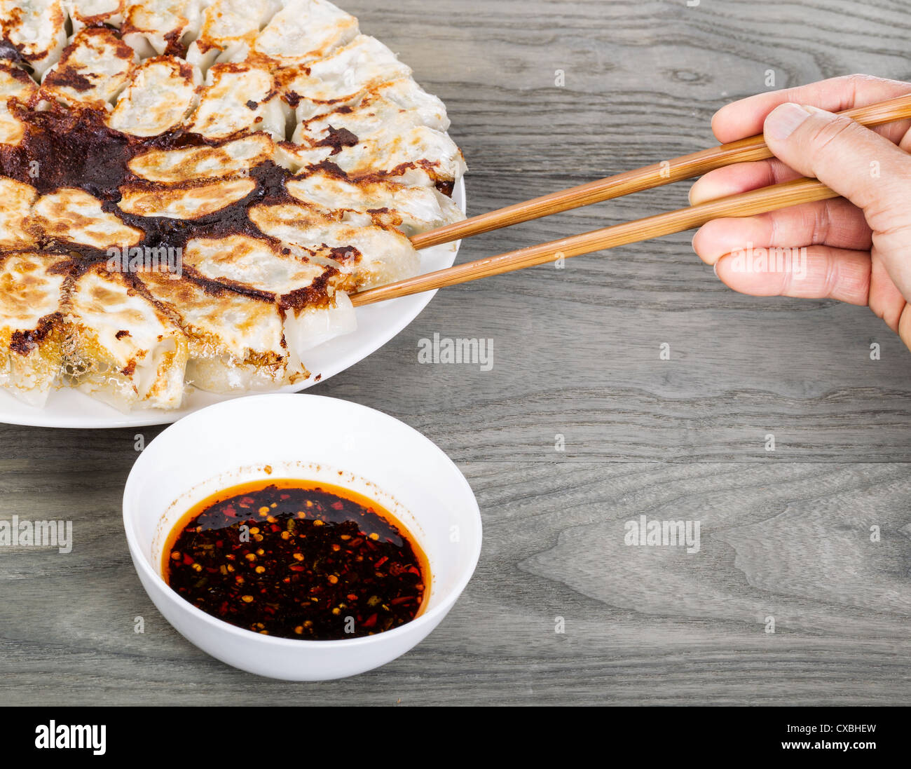 Hand holding chopsticks with Chinese dumplings on white plate with wood table in background Stock Photo