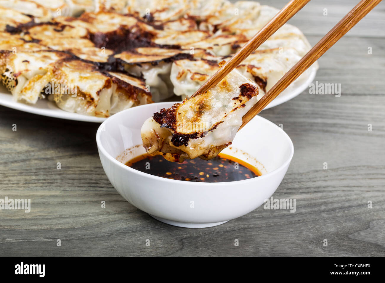 Freshly cooked Chinese dumplings with chopsticks, small white bowl and plate in background Stock Photo