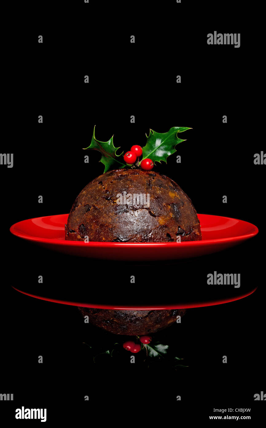 Photo of a traditional Christmas pudding with holly and berries on top, on a black background. Stock Photo