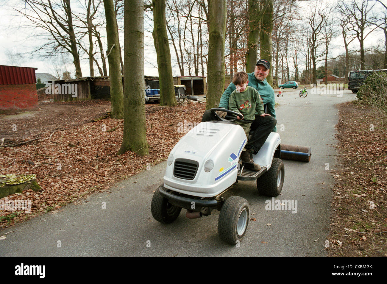 Father with son on a lawn tractor pulling a roll Germany Stock
