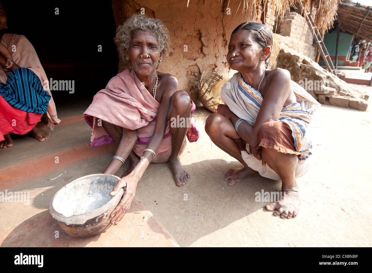 Two Desia Kondh tribal women squatting outside their village house holding welcome bowl of ash, Bissam Cuttack, Orissa, India Stock Photo