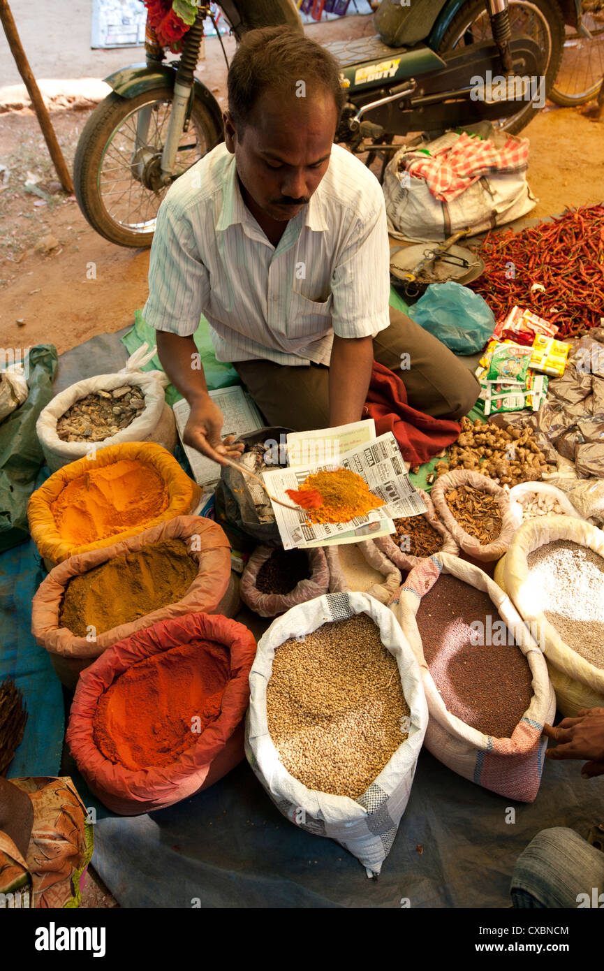 Spice stall at Desia Kondh tribal market, man spooning turmeric, cumin and chilli powder for customer, near Rayagada, Orissa Stock Photo