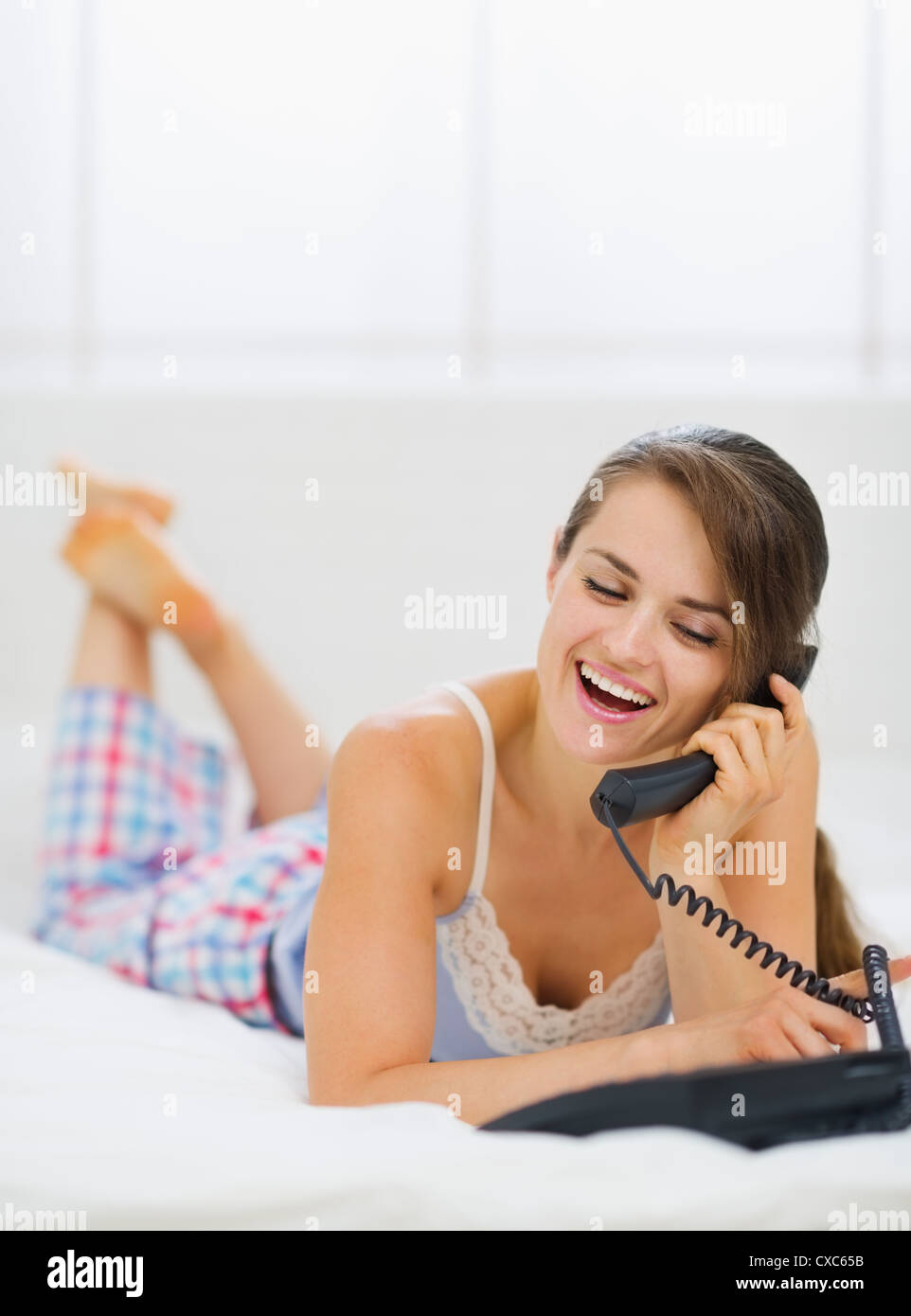 Happy young woman laying in bed and making phone call Stock Photo