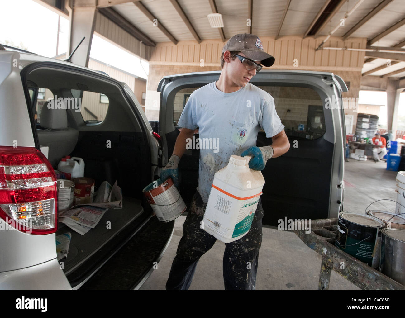 Male employee at the City of Austin household hazardous waste facility unloads paint from resident to properly dispose of Stock Photo