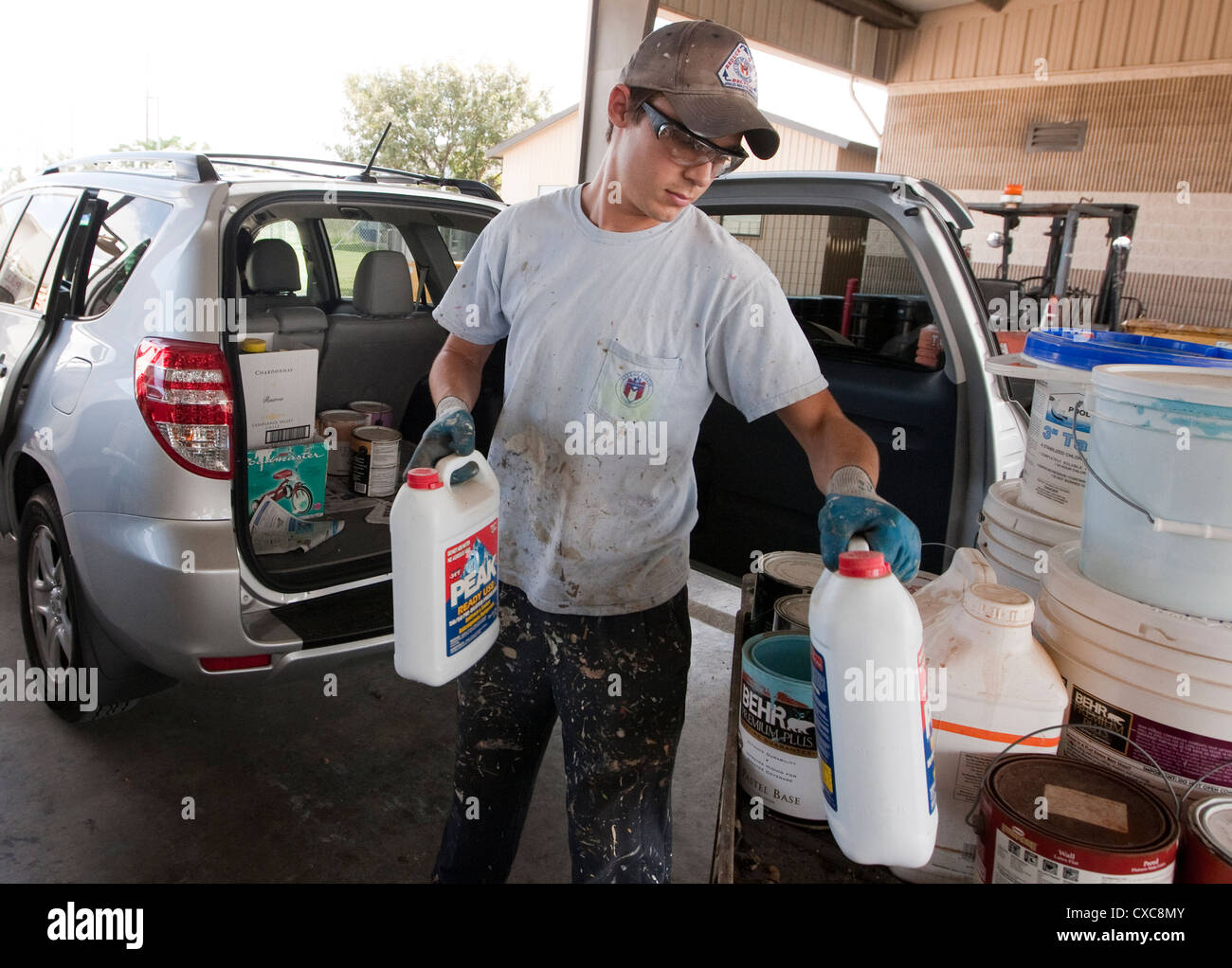 Male employee at the City of Austin household hazardous waste facility unloads paint from resident to properly dispose of Stock Photo