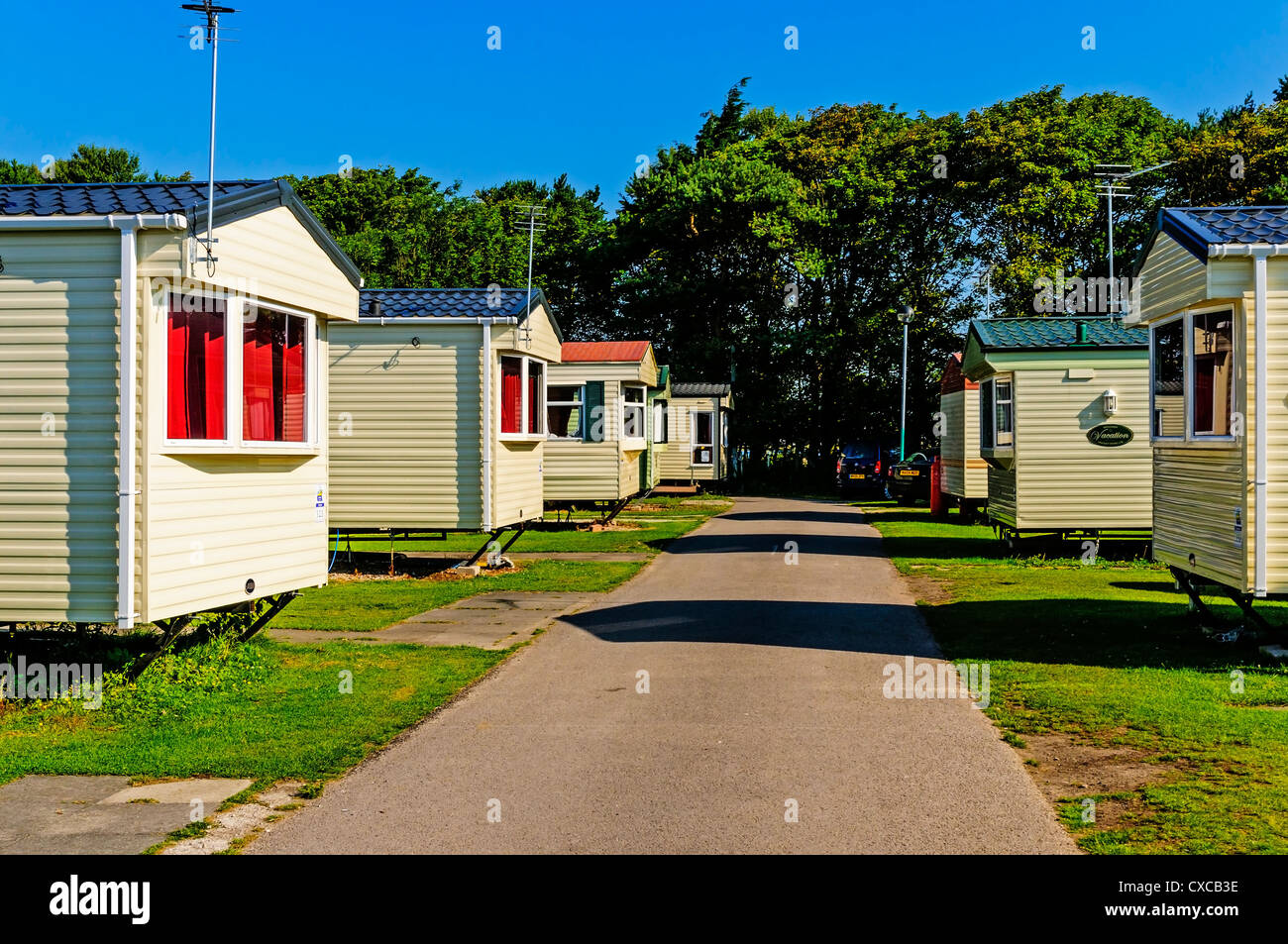Cream coloured caravans smartly arranged on either side of a pink tinted road contrast strongly with an intensely blue sky, Stock Photo