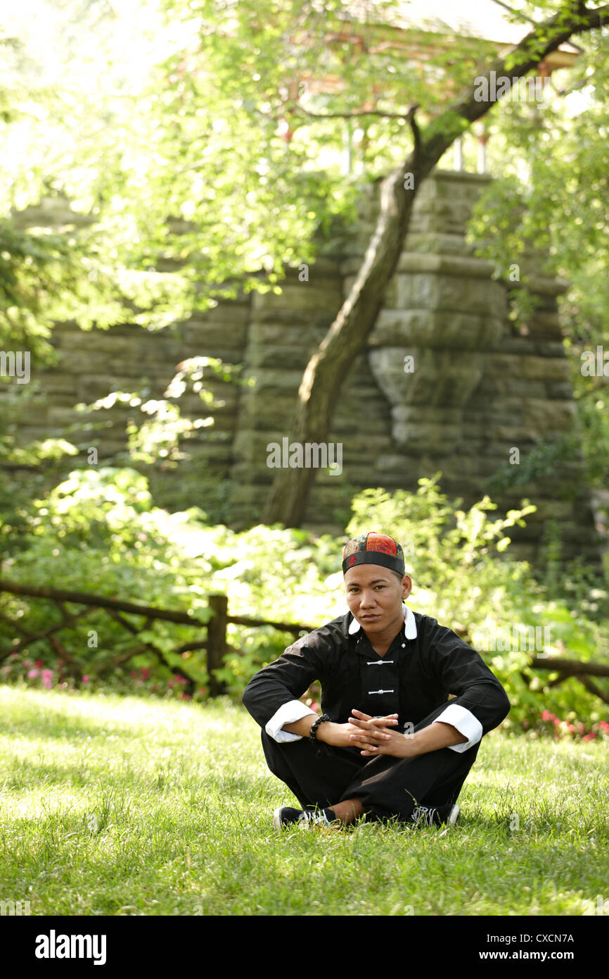 Man in traditional Asian clothing sitting in grass Stock Photo