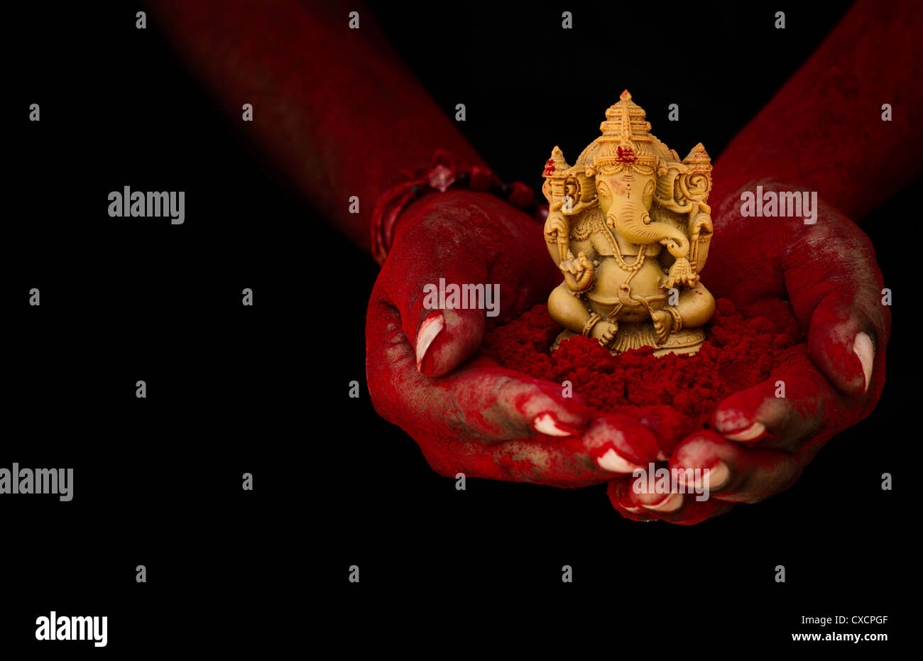Hindu Elephant God. Red powder covered indian mans hand holding Lord Ganesha statue against black background Stock Photo