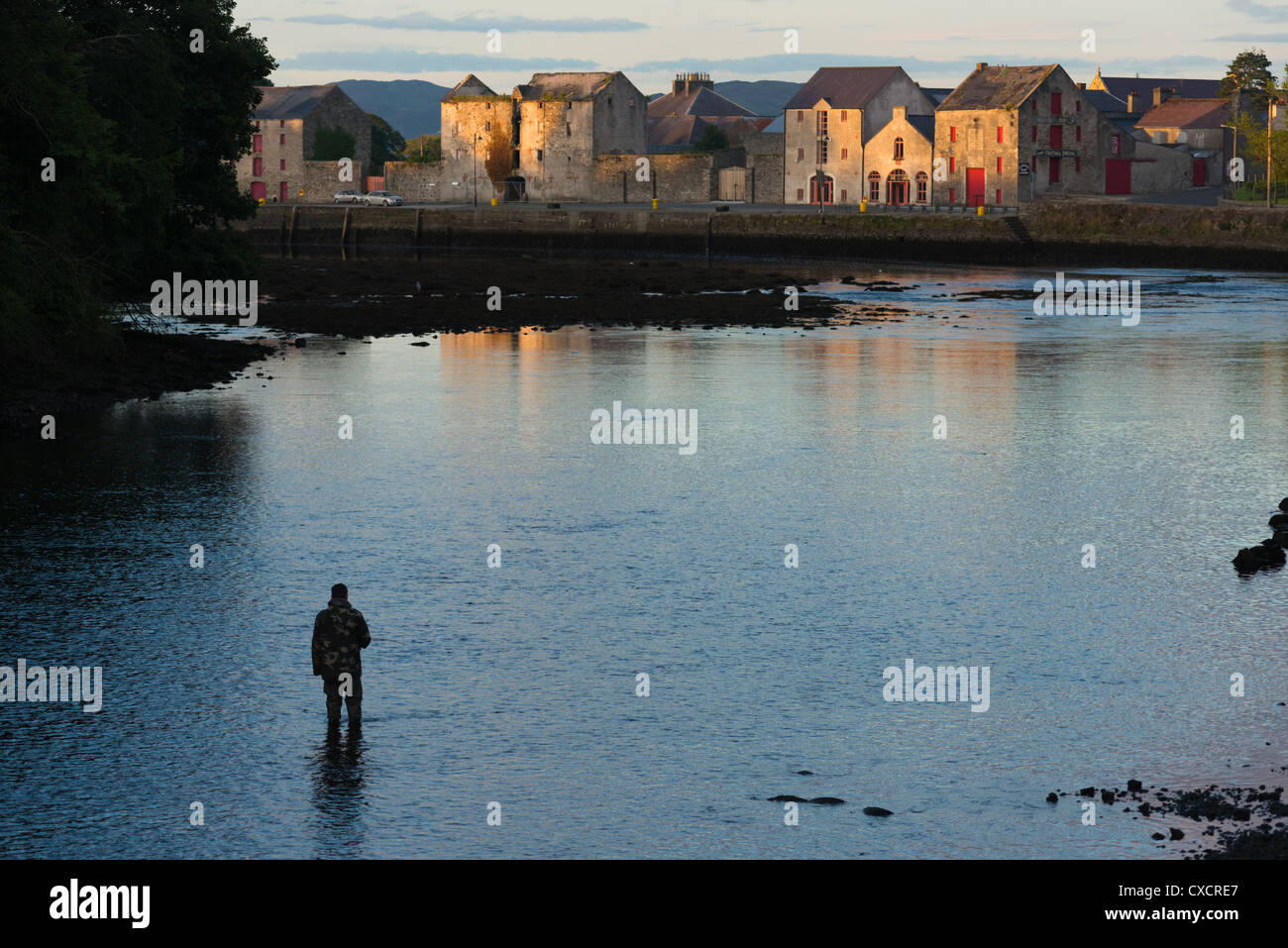 Man fishing with view of warehouses on the waterfront, Ramelton, County Donegal, Ulster Province, Republic of Ireland. Stock Photo