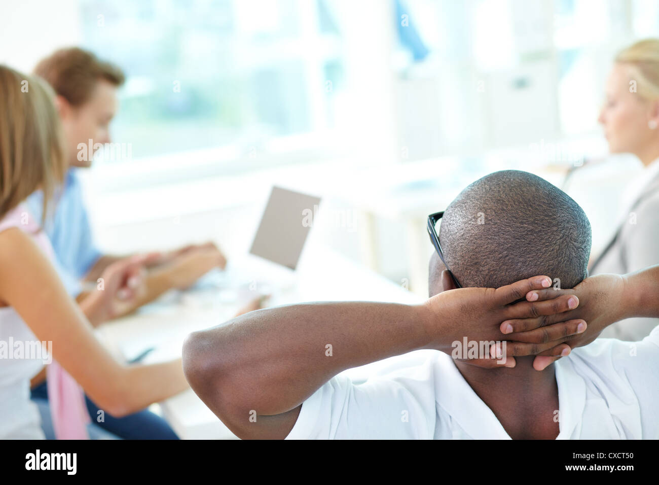 Rear view of relaxed teacher keeping hands behind head and looking at ...