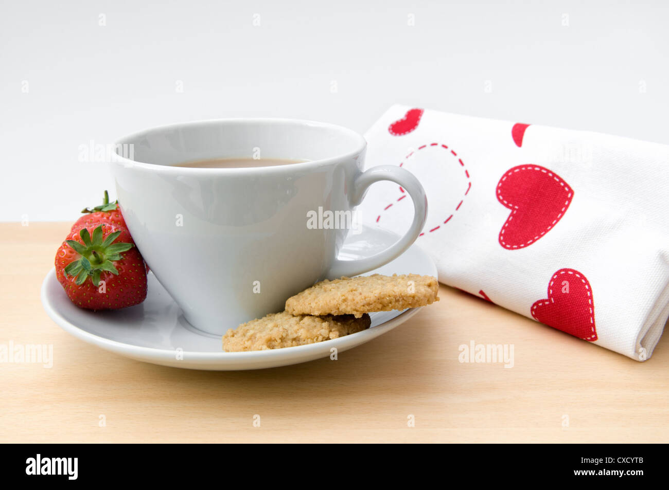 Cup of tea with strawberries and biscuits on the side with red and white napkin on table top Stock Photo