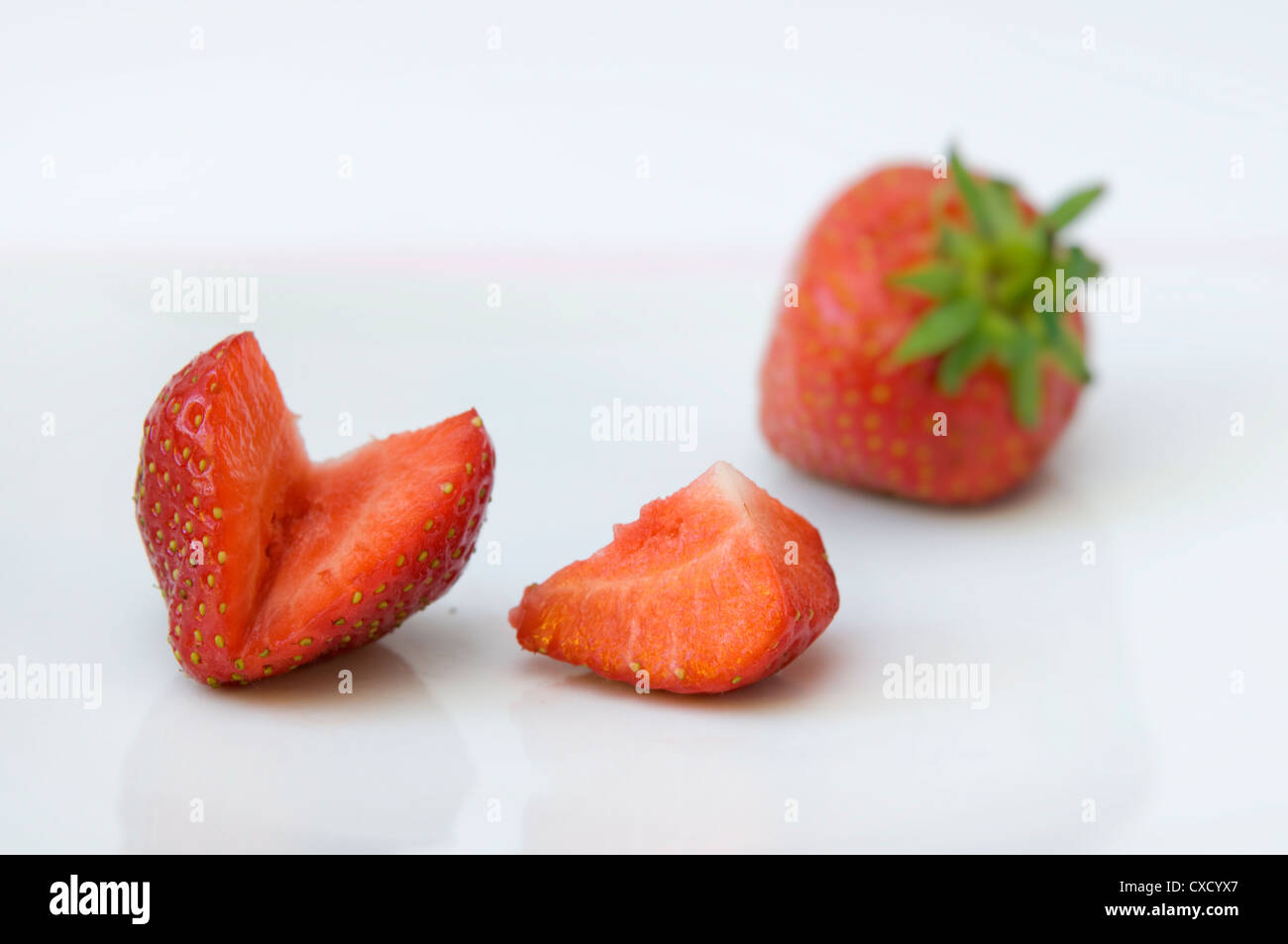 Strawberries on white plate, one of which is sliced Stock Photo