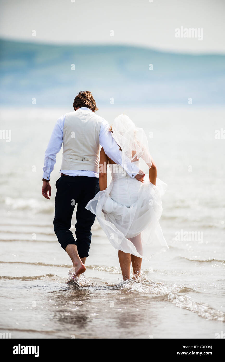 a newly married bride and groom paddling in sea after their wedding on a summer afternoon, Ynyslas beach, Ceredigion Wales UK Stock Photo