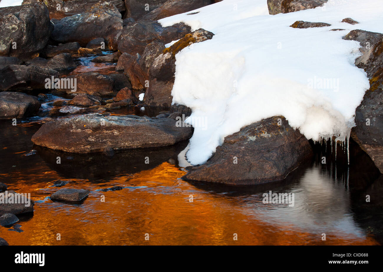 Warm light from the sun hitting rocks and snow around the edge of a ...