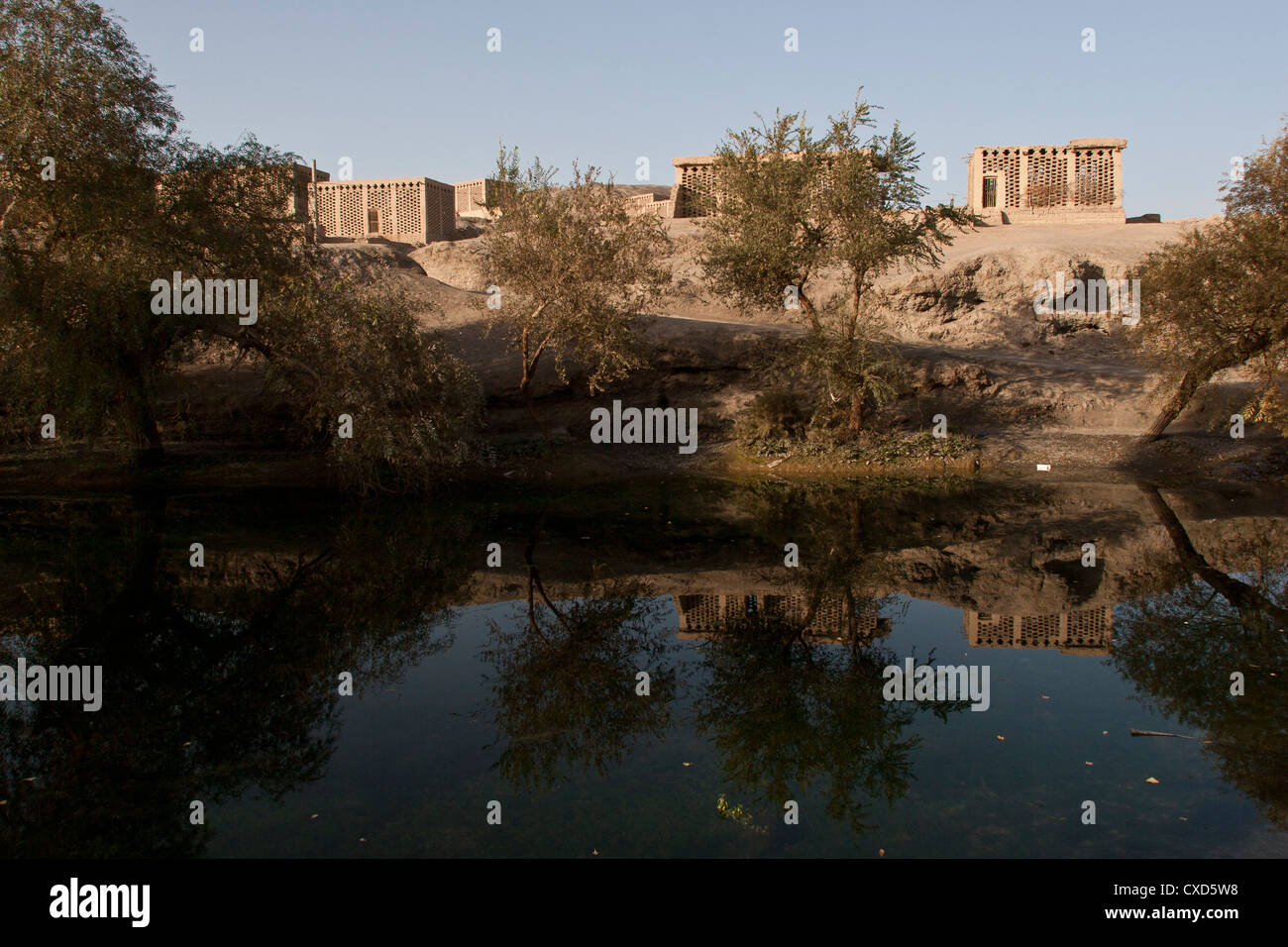 Small earth brick houses used as grape drying sheds on a hill above a pond in Turpan, Xinjiang, China Stock Photo