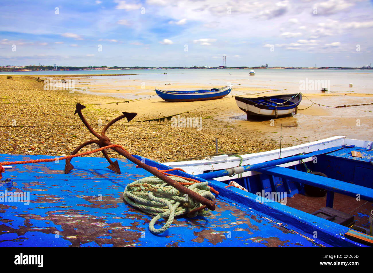 Old blue fishing boats in a beach and rusty anchor in the foreground Stock Photo