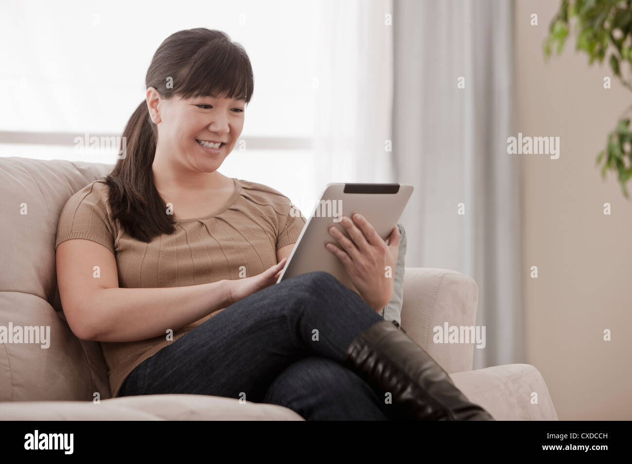 Asian woman sitting on sofa using digital tablet Stock Photo - Alamy