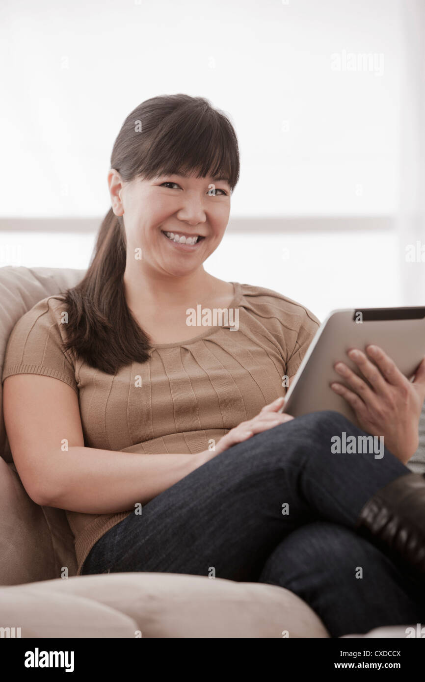 Asian woman sitting on sofa using digital tablet Stock Photo - Alamy