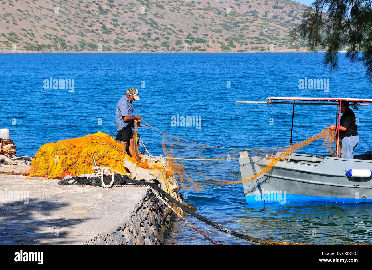 Two Cretan fishermen  tending  and preparing fishing nets for the evening fishing in their caiques, Elounda, Crete Stock Photo