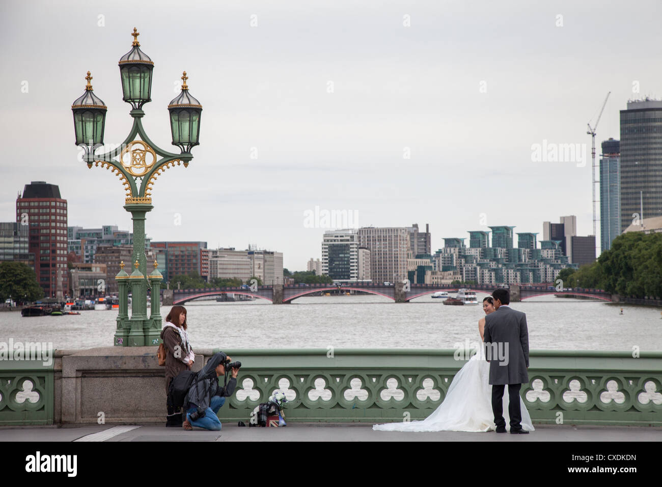 A bride and groom pose for wedding photographs on Westminster Bridge London with Lambeth Bridge in background Stock Photo