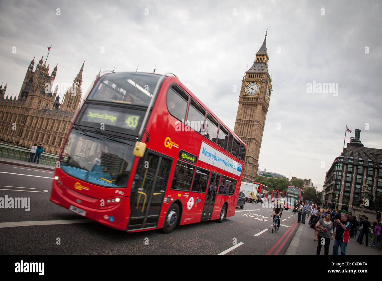 A classic red double-decker bus driving across Westminster Bridge in London, with Big Ben and the Houses of Parliament visible in the background on a slightly overcast day.
